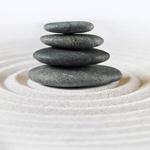 Pile of small round black stones balanced on top of each other on white sand.