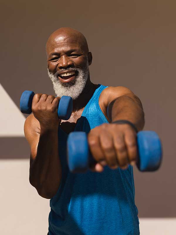 Older African American man smiling while holding dumbbells exercising.