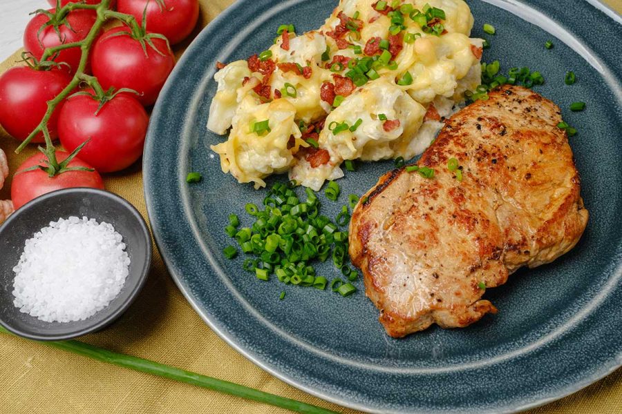 Low-carb pork chops with cauliflower au gratin served on a dark blue dinner plate.